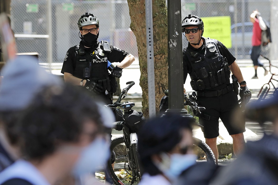 FILE - In this July 20, 2020, file photo, police officers look on at protesters in Seattle. The Seattle City Council is scheduled to take votes Monday, Aug. 10, 2020, on proposals that would reduce the police department by up to 100 officers through layoffs and attrition, actions supported by demonstrators who have marched in the city following George Floyd's killing in Minneapolis but strongly opposed by the mayor and police chief. (AP Photo/Elaine Thompson, File)