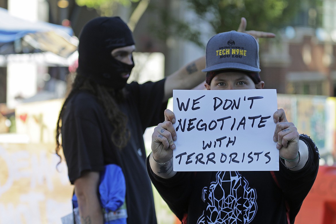A protester holds a sign that reads "We don't negotiate with terrorists," Friday, June 26, 2020 inside the the CHOP (Capitol Hill Occupied Protest) zone in Seattle after workers and trucks from the Seattle Department of Transportation arrived with the intention of removing barricades that had been set up in the area which has been occupied by protesters since Seattle Police pulled back from their East Precinct building following violent clashes with demonstrators earlier in the month. (AP Photo/Ted S. Warren)