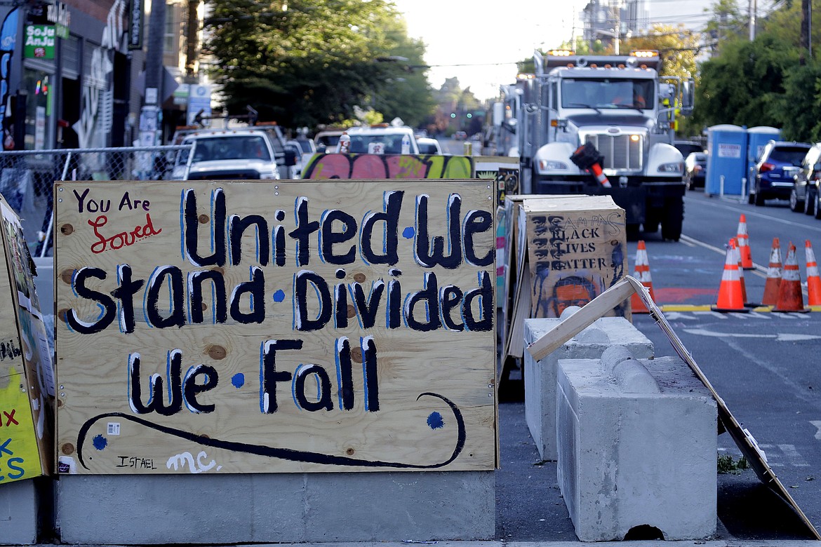 A sign on a barricade reads "United we stand divided we fall," as a truck and other heavy equipment from the Seattle Department of Transportation is staged at the the CHOP (Capitol Hill Occupied Protest) zone in Seattle, Friday, June 26, 2020. Workers arrived with the intention of removing barricades that had been set up in the area and were met with opposition from protesters. Several blocks in the area have been occupied by protesters since Seattle Police pulled back from their East Precinct building following violent clashes with demonstrators earlier in the month. (AP Photo/Ted S. Warren)