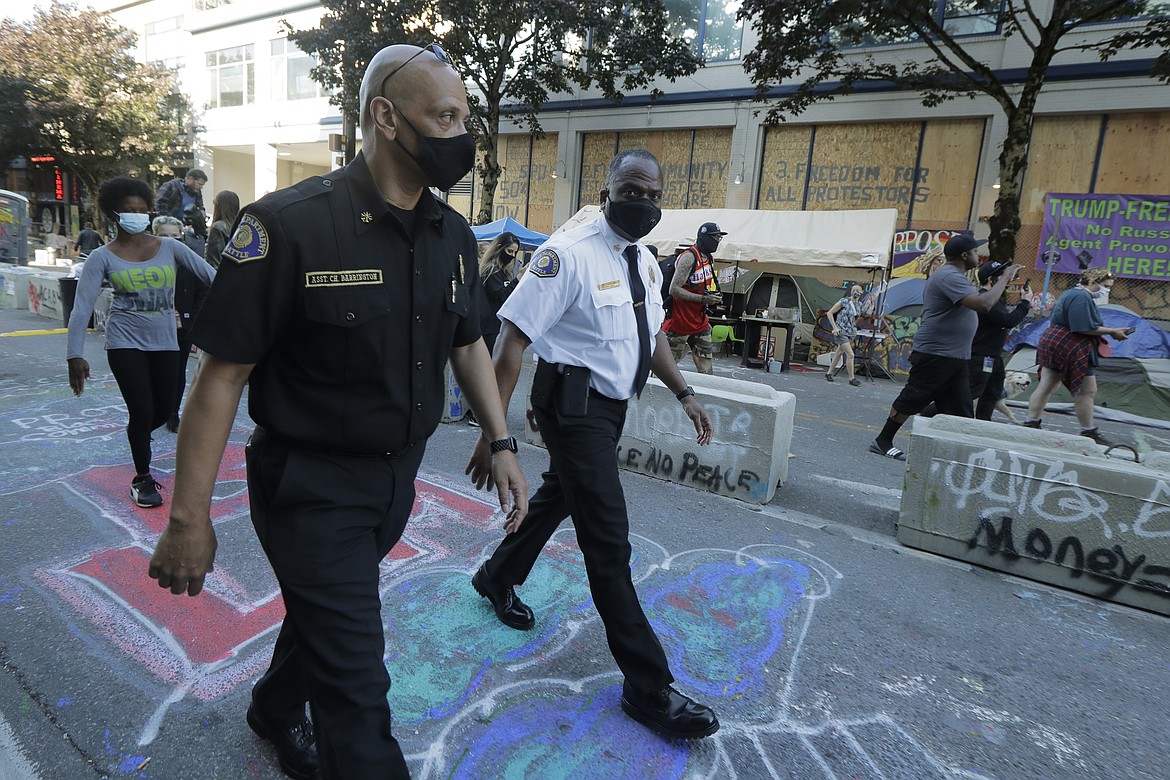 Seattle Fire Chief Harold Scoggins, right, and Assistant Chief Willie Barrington, left, walk, Friday, June 26, 2020 inside the CHOP (Capitol Hill Occupied Protest) zone in Seattle. The officials were on hand to try and negotiate with protesters after workers and trucks from the Seattle Department of Transportation who had arrived with the intention of removing barricades were met with resistance. The area has been occupied by protesters since Seattle Police pulled back from their East Precinct building following violent clashes with demonstrators earlier in the month. (AP Photo/Ted S. Warren)