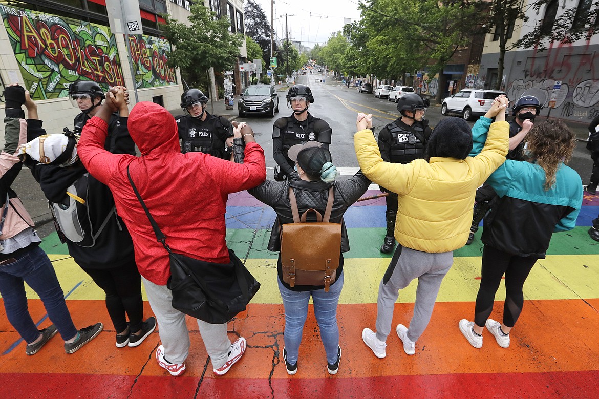 Protesters standing on a rainbow-themed crosswalk holding hands in front of a line of police officers blocking a street Wednesday, July 1, 2020, in Seattle, where streets had been blocked off in an area demonstrators had occupied for weeks. Seattle police showed up in force earlier in the day at the "occupied" protest zone, tore down demonstrators' tents and used bicycles to herd the protesters after the mayor ordered the area cleared following two fatal shootings in less than two weeks. The "Capitol Hill Occupied Protest" zone was set up near downtown following the death of George Floyd while in police custody in Minneapolis. (AP Photo/Elaine Thompson)
