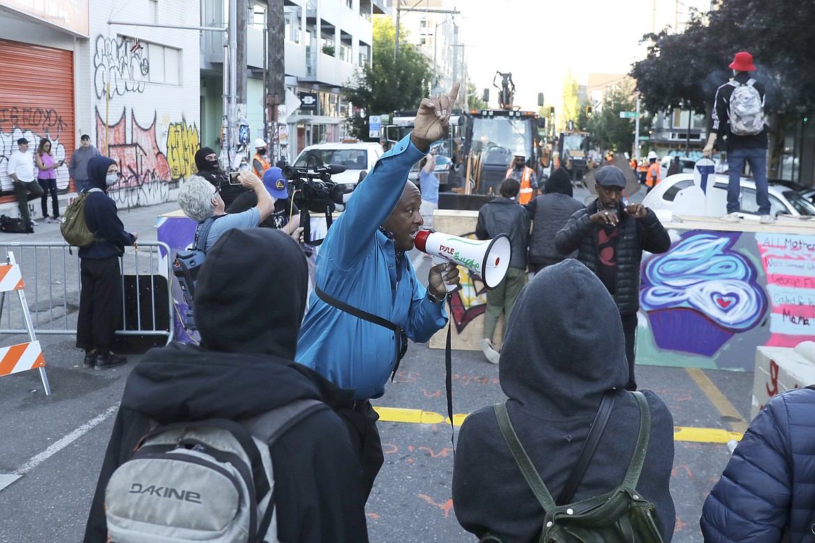 A man speaking in to a bullhorn urges protesters not to be violent after workers and heavy equipment from the Seattle Department of Transportation arrived at the the CHOP (Capitol Hill Occupied Protest) zone in Seattle, Friday, June 26, 2020, with the intention of removing barricades that had been set up in the area. Several blocks in the area have been occupied by protesters since Seattle Police pulled back from their East Precinct building following violent clashes with demonstrators earlier in the month. (AP Photo/Ted S. Warren)