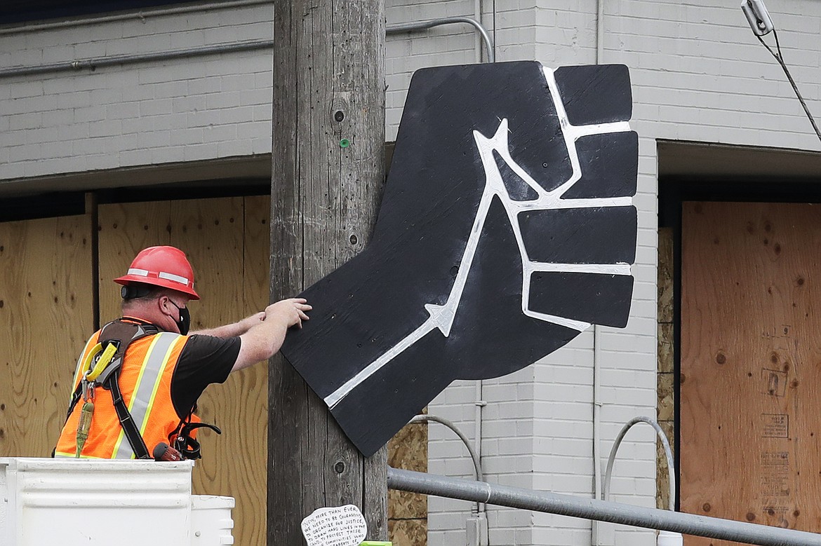 A worker removes a rendering of a clenched fist from a Seattle police precinct Wednesday, July 1, 2020, in Seattle, where streets had been blocked off in an area demonstrators had occupied for weeks. Seattle police showed up in force earlier in the day at the "occupied" protest zone, tore down demonstrators' tents and used bicycles to herd the protesters after the mayor ordered the area cleared following two fatal shootings in less than two weeks. The "Capitol Hill Occupied Protest" zone was set up near downtown following the death of George Floyd while in police custody in Minneapolis. (AP Photo/Elaine Thompson)