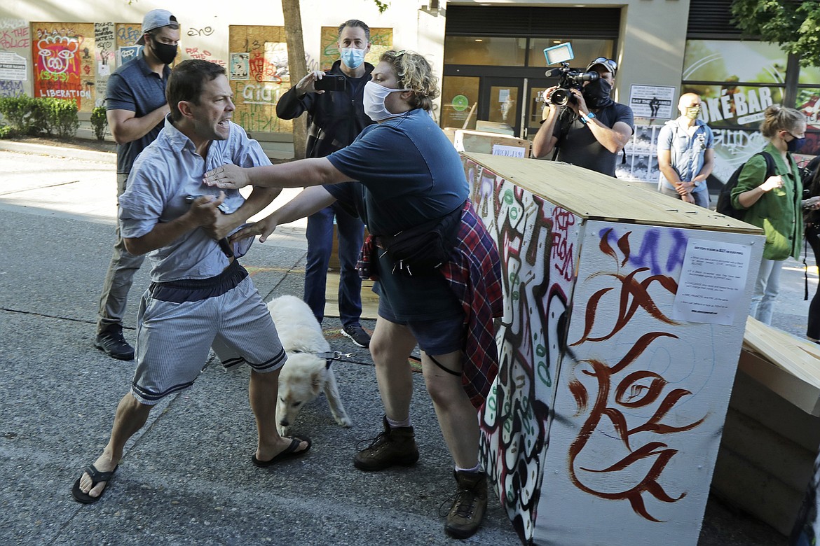 A person tries to take away a hammer from a man at left who was using it to remove artwork on barricades Friday, June 26, 2020 at the CHOP (Capitol Hill Occupied Protest) zone in Seattle. The man lives in a house in the same block and said he was tired of protesters occupying his neighborhood. Also on Friday Seattle Department of Transportation workers arrived with the intention of removing barricades that had been set up in the area, but left after being met with resistance from protesters. (AP Photo/Ted S. Warren)