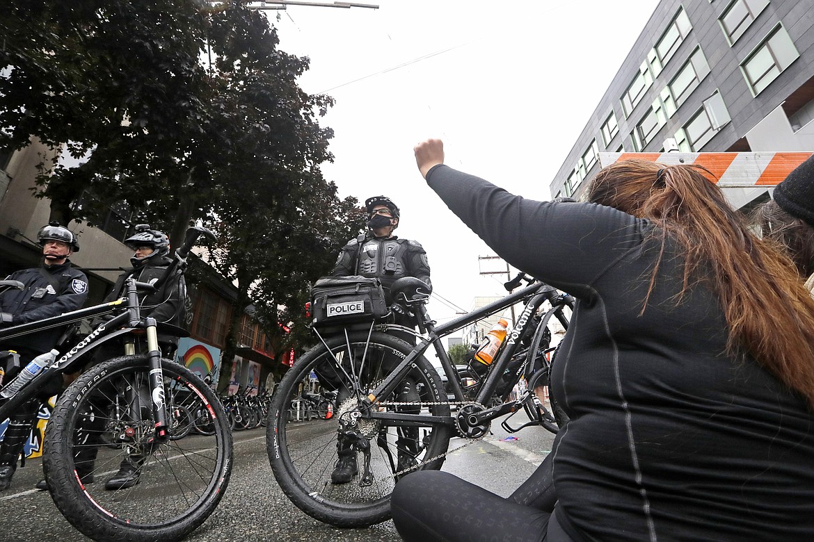 A woman sits in the street as police officers block a street in an area police cleared hours earlier Wednesday, July 1, 2020, in Seattle, where streets had been blocked off in an area demonstrators had occupied for weeks. Seattle police arrived in force earlier in the day at the "Capitol Hill Occupied Protest" zone set up after the death of George Floyd in Minneapolis police custody, and they tore down demonstrators' tents and used bicycles to herd the protesters after the mayor ordered the area cleared following two fatal shootings in less than two weeks. (AP Photo/Elaine Thompson)
