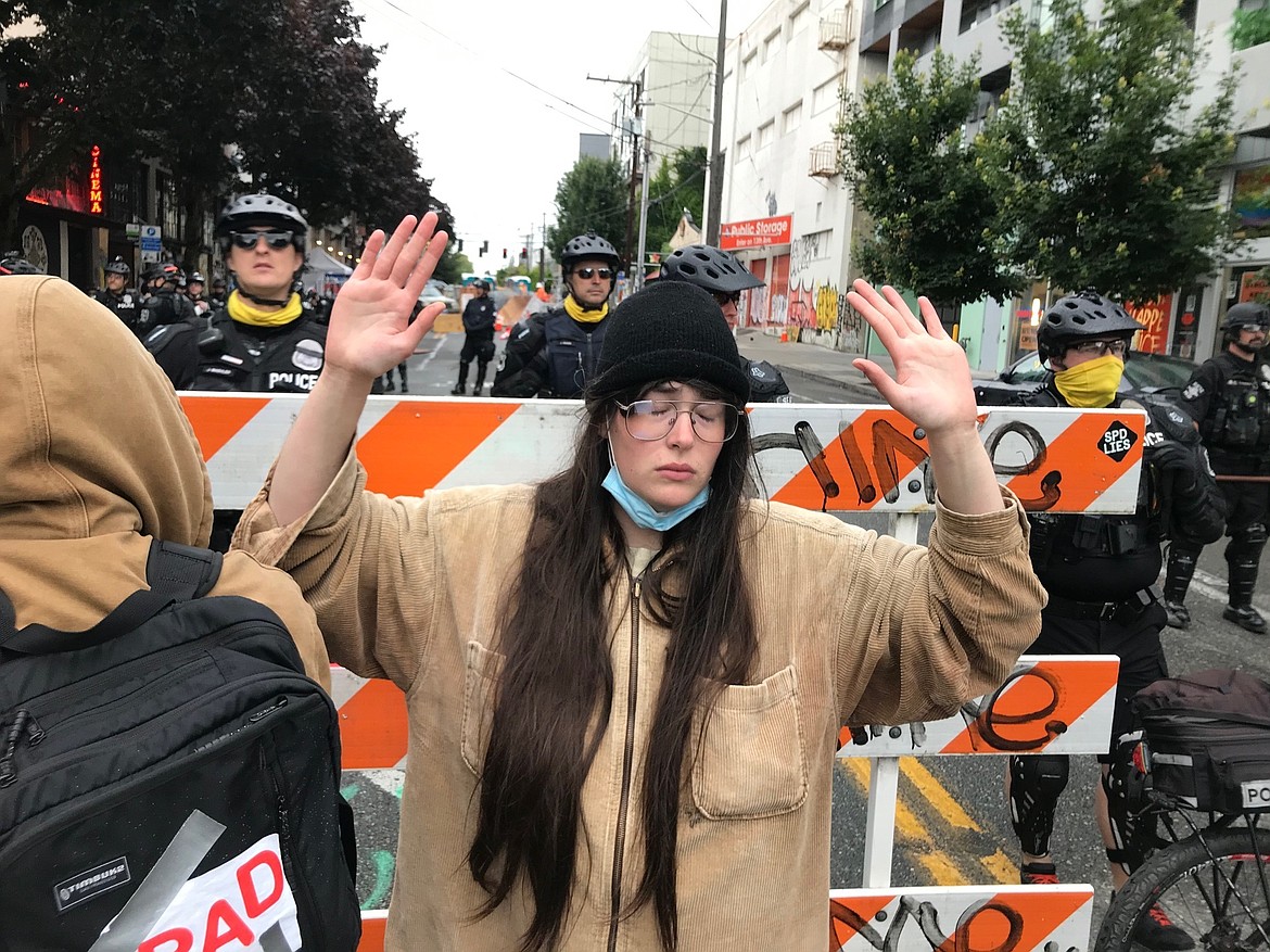 A protester stands with her hand up in front of a road blocked by Seattle police in the Capitol Hill Organized Protest zone early Wednesday, July 1, 2020. Police in Seattle have torn down demonstrators' tents in the city's so-called occupied protest zone after the mayor ordered it cleared. (AP Photo/Aron Ranen)