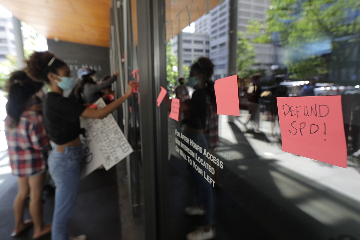 Protesters put adhesive notes on the doors of Seattle City Hall, Monday, July 13, 2020, following a news conference held by Mayor Jenny Durkan. Durkan and Police Chief Carmen Best were critical of a plan backed by several city council members that seeks to cut the police department's budget by 50 percent. (AP Photo/Ted S. Warren)