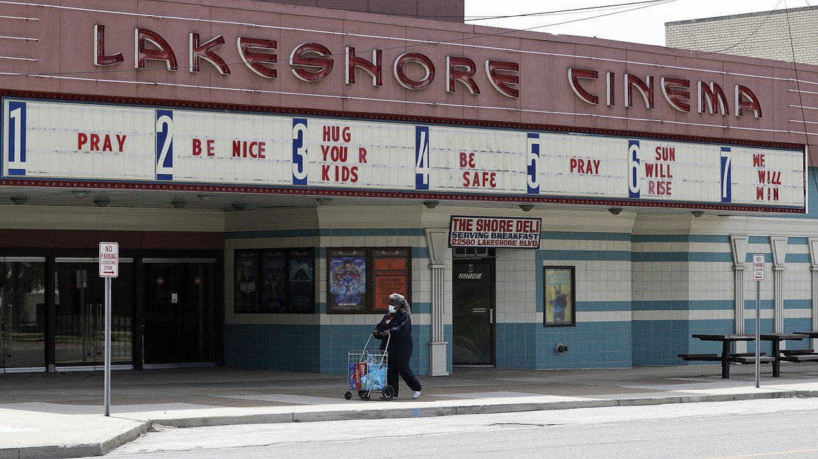 A woman wearing a mask walks with her groceries past a closed Lakeshore Cinema theatre, Wednesday, May 6, 2020, in Euclid, Ohio. With the economy paralyzed by business closures, the unemployment rate likely jumped to at least 16% — from just 4.4% in March — and employers cut a stunning 21 million or more jobs just in April, economists have forecast.  (AP Photo/Tony Dejak)