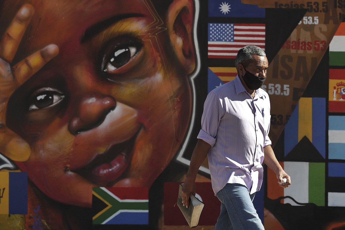 A man wearing a mask amid the COVID-19 pandemic carries a Bible in Ceilandia, one of the neighborhoods most affected by COVID-19 in Brasilia, Brazil, Tuesday, July 21, 2020. (AP Photo/Eraldo Peres)