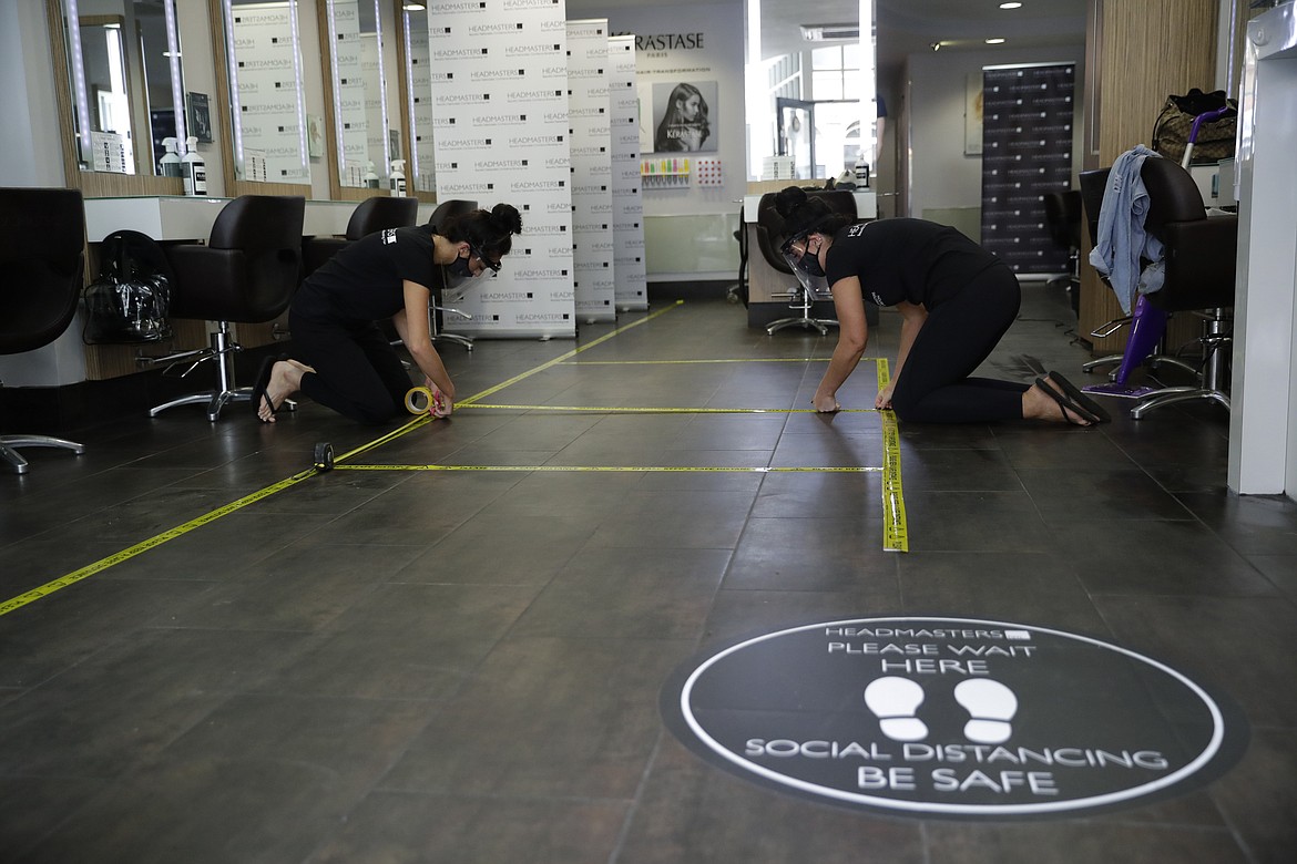 Salon owner Sian Rose Maclaren, right, and one of her managers measure and stick down tape to mark out social distancing lines as they try out wearing their new face shields and masks whilst preparing to reopen at a franchise branch of the Headmasters group of hairdressing salons, in Surbiton, south west London, Thursday, July 2, 2020. Millions of people in Britain will be able to go to the pub, visit a movie theater, get a haircut or attend a religious service starting July 4, in a major loosening of coronavirus lockdown restrictions. (AP Photo/Matt Dunham)