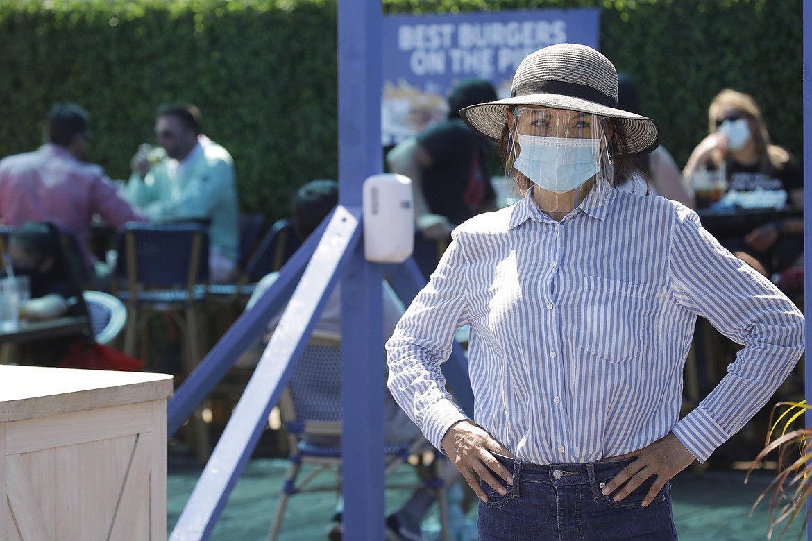 A hostess waits to sit customers on a restaurant at the pier Sunday, July 12, 2020, in Santa Monica, Calif., amid the coronavirus pandemic. A heat wave has brought crowds to California's beaches as the state grappled with a spike in coronavirus infections and hospitalizations. (AP Photo/Marcio Jose Sanchez)