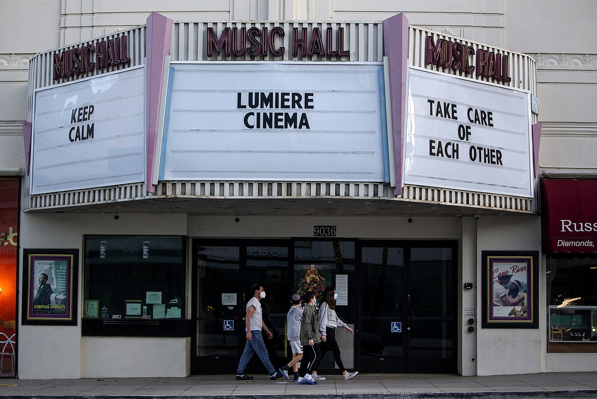 A family wears mask as they walk under the Lumiere Cinema at the Music Hall in Beverly Hills, Calif., on Wednesday, April 15, 2020. The world's biggest economy began issuing one-time payments this week to tens of millions of people as part of its $2.2 trillion coronavirus relief package, with adults receiving up to $1,200 each and $500 per child to help them pay the rent or cover other bills. The checks will be directly deposited into accounts or mailed to households in the coming weeks, depending on how people filed their tax returns. (AP Photo/Damian Dovarganes)
