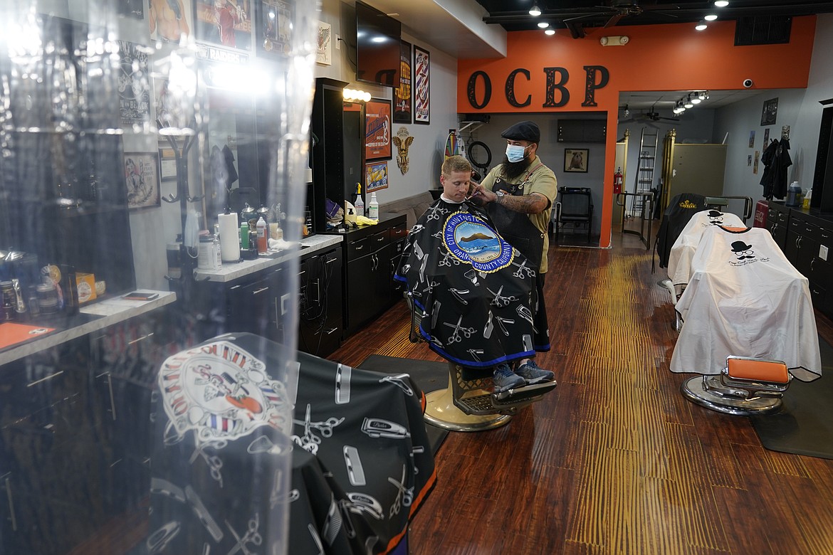 Luis Lopez gives a hair cut to Marty Broser behind a plastic curtain at Orange County Barbers Parlor, Wednesday, May 27, 2020, in Huntington Beach, Calif. Orange County Barber shops and salons were allowed to open today. (AP Photo/Ashley Landis)