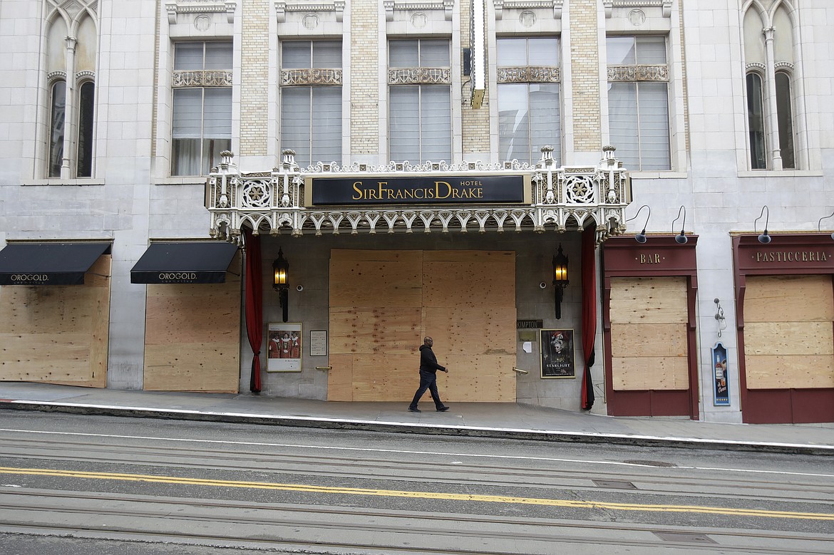 A man walks in front of boarded windows and an entrance to the Sir Francis Drake Hotel in San Francisco, Sunday, March 29, 2020. Californians endured a weekend of stepped-up restrictions aimed at keeping them home as much as possible while hospitals and health officials scrambled Sunday to ready themselves for a week that could see the feared dramatic surge in coronavirus cases. (AP Photo/Jeff Chiu)