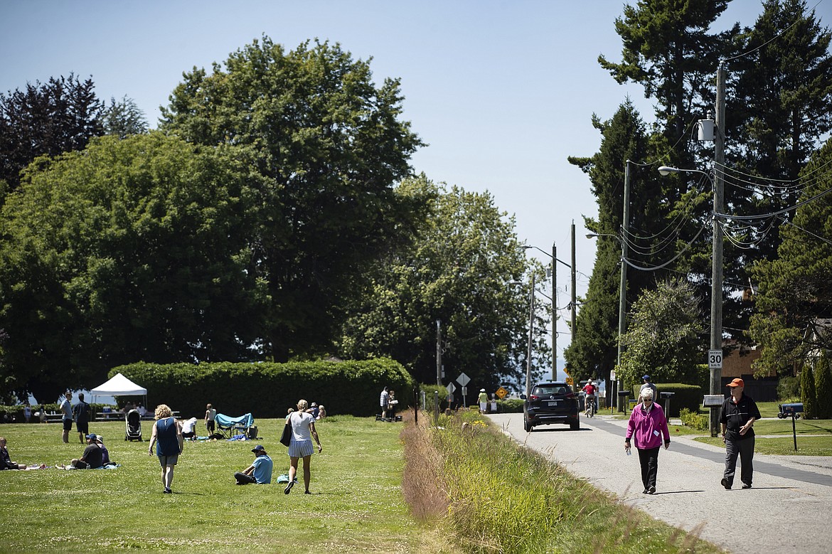 A ditch marks the Canada-U.S. border and separates people walking on the road, right, in Surrey, British Columbia, and those gathered at Peace Arch Historical State Park, left, in Blaine, Wash., Sunday, July 5, 2020. Although the B.C. government closed the Canadian side of the park in June due to concerns about crowding and COVID-19, people are still able to meet in the U.S. park due to a treaty signed in 1814 that allows citizens of Canada and the U.S. to unite in the park without technically crossing any border. (Darryl Dyck/The Canadian Press via AP)