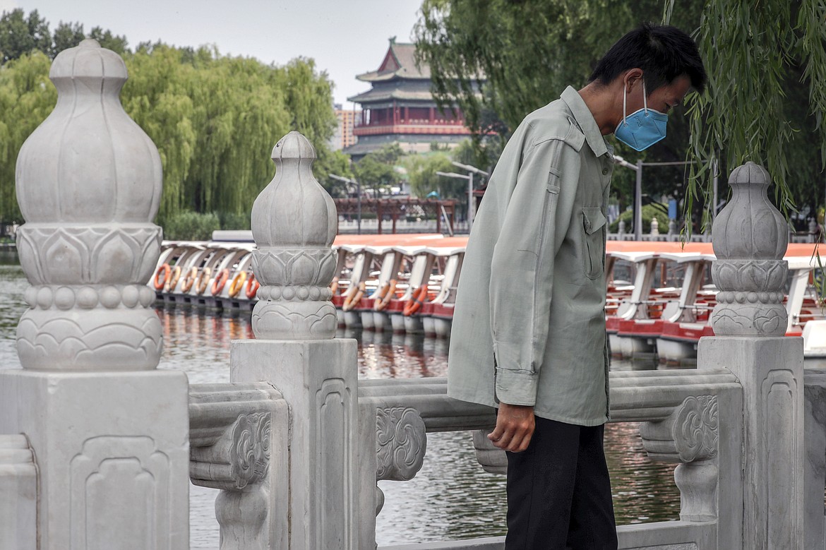 A man wearing a protective face mask to help curb the spread of the coronavirus stands against a roll of boats parked on the barricaded Houhai Lake, a usually popular tourist spot before the new coronavirus outbreak in Beijing, Tuesday, June 30, 2020. China, where the coronavirus pandemic began in December, was the first economy to reopen in March after the ruling Communist Party declared victory over the disease. Manufacturing and other activity is reviving but demand for exports is feeble and Chinese consumers, worried about losing jobs, are reluctant to spend. (AP Photo/Andy Wong)