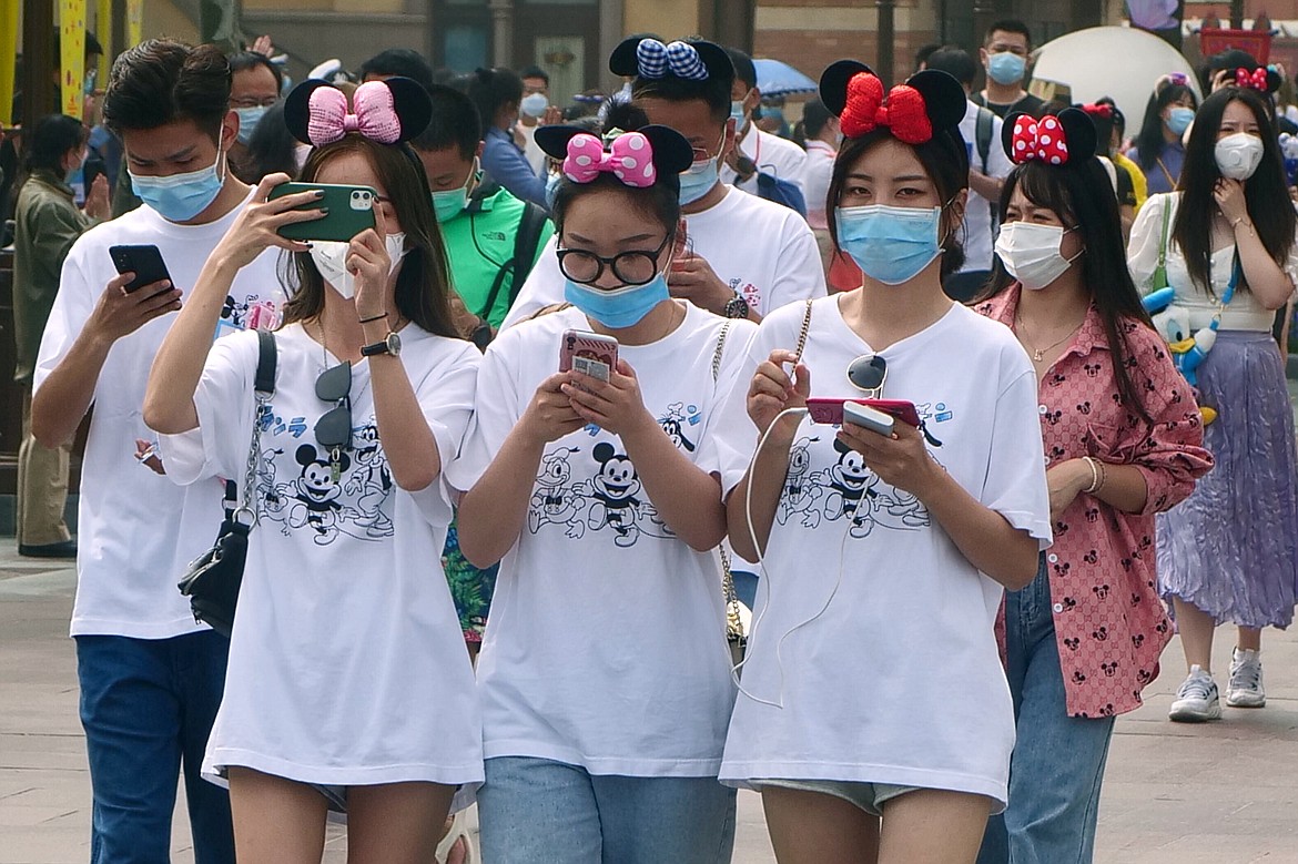 Visitors, wearing face masks, enter the Disneyland theme park in Shanghai as it reopened, Monday, May 11, 2020. Visits will be limited initially and must be booked in advance, and the company said it will increase cleaning and require social distancing in lines for the various attractions.(AP Photo/Sam McNeil)