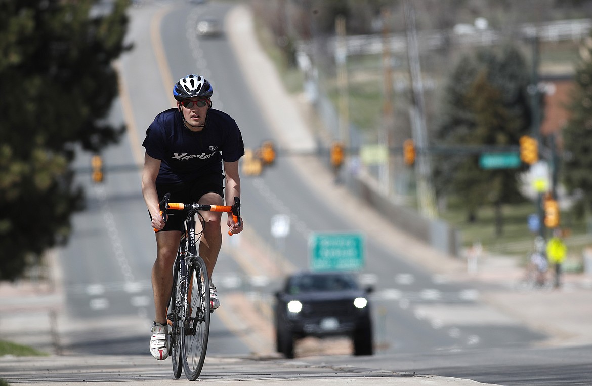 Bicyclist Elliot Steinberg, a student at Xavier University in Cincinnati, rides a bicycle up a hill along nearly-empty University Boulevard as a statewide stay-at-home order remains in effect in an effort to reduce the spread of the coronavirus Sunday, April 5, 2020, in Cherry Hills Village, Colo. (AP Photo/David Zalubowski)