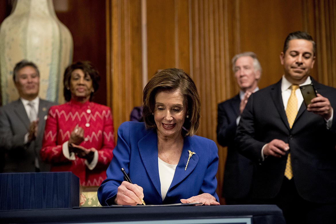 House Speaker Nancy Pelosi of Calif., accompanied by bipartisan legislators, signs the Coronavirus Aid, Relief, and Economic Security (CARES) Act after it passed in the House on Capitol Hill, Friday, March 27, 2020, in Washington. The $2.2 trillion package will head to head to President Donald Trump for his signature. (AP Photo/Andrew Harnik)