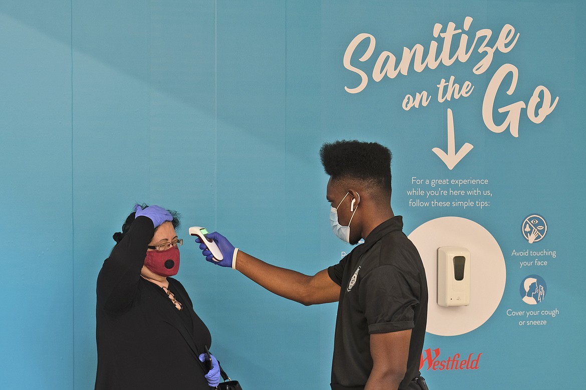 FILE - In this Monday, June 29, 2020, file photo, Bigard Ogbonna, right, checks a customer's temperature before they enter a store at the Garden State Plaza mall in Paramus, N.J., as New Jersey's indoor shopping malls reopened from their COVID-19 pause. U.S. employers likely rehired several million more workers in June, thereby reducing a Depression-level unemployment rate, but the most up-to-date data suggests that a resurgent coronavirus will limit further gains. (AP Photo/Seth Wenig, File)