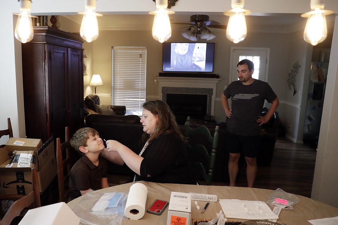 Mendy McNulty swabs the nose of her son, Hudson, 9, in their home in Mount Juliet, Tenn., Tuesday, July 28, 2020. Her husband, Joe, right, waits his turn. The family is participating in testing done twice a month to help answer some of the most vexing questions about the coronavirus. (AP Photo/Mark Humphrey)