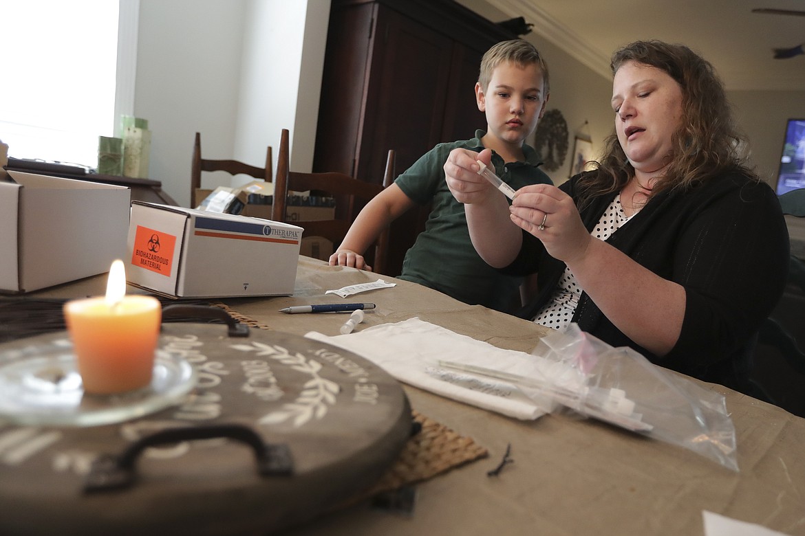 Mendy McNulty prepares test swabs for shipping as her son, Andrew, 7, watches after the family did a twice-weekly coronavirus test in their home Tuesday, July 28, 2020, in Mount Juliet, Tenn. Six thousand U.S. parents and kids are swabbing their noses twice a week to answer some of the most vexing mysteries about the coronavirus. (AP Photo/Mark Humphrey)