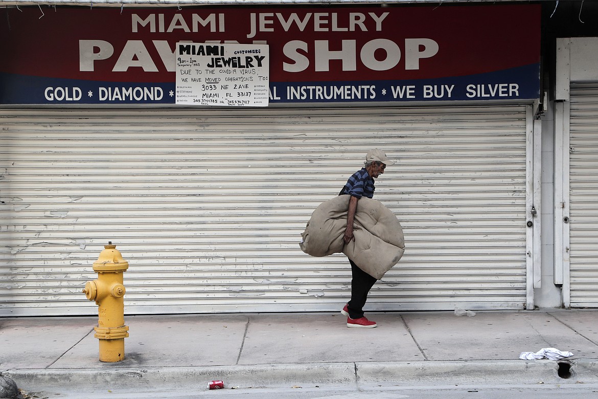 A homeless man carrying his bedding walks past the Miami Jewelry Pawn Shop during the new coronavirus pandemic, Thursday, May 7, 2020, in Miami. The U.S. government is poised to report the worst set of job numbers since record-keeping began in 1948, a stunning snapshot of the toll the coronavirus has taken on a now-shattered economy. (AP Photo/Lynne Sladky)
