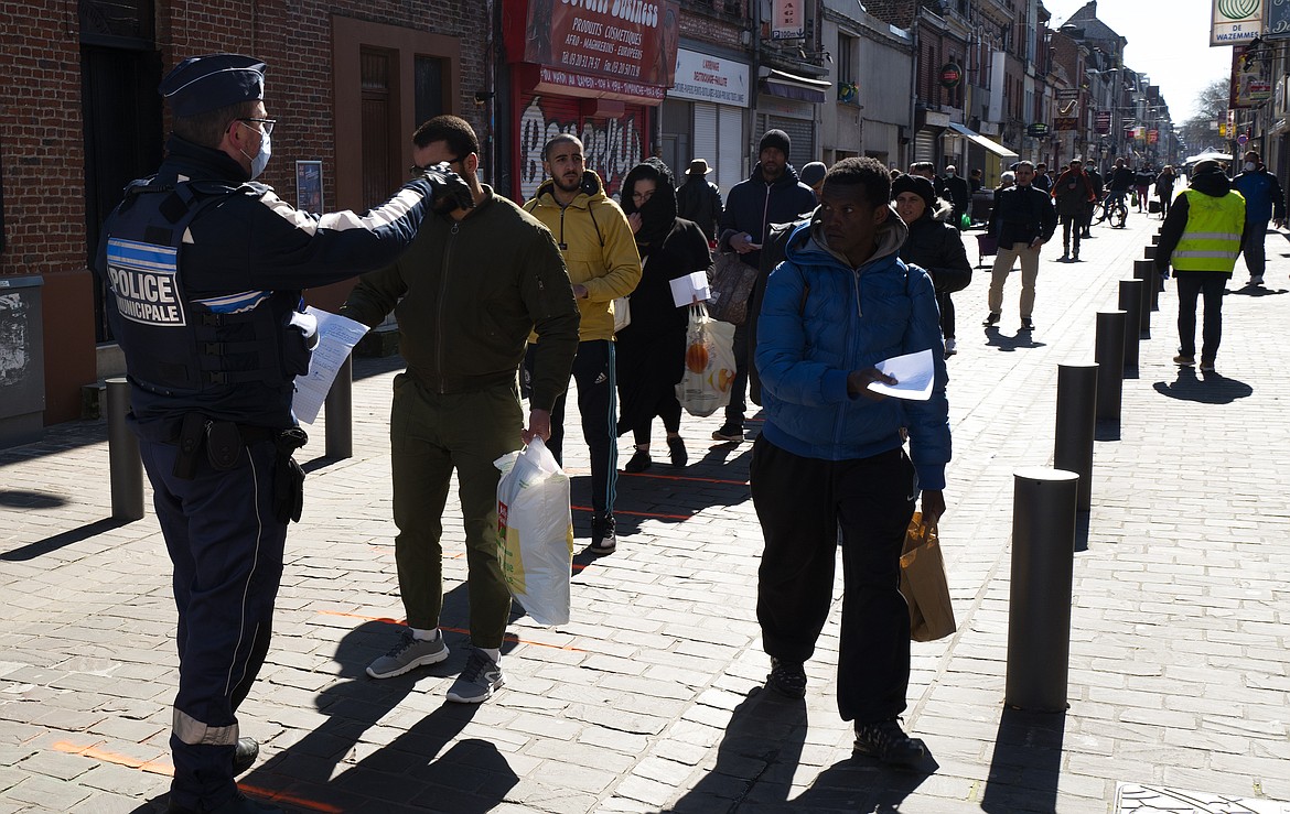 A city police officer checks residents at an open air market in Lille, northern France Sunday, March 22, 2020. French President Emmanuel Macron urged employees to keep working in supermarkets, production sites and other businesses that need to keep running amid stringent restrictions of movement due to the rapid spreading of the new coronavirus in the country.  For most people, the new coronavirus causes only mild or moderate symptoms. For some it can cause more severe illness. (AP Photo/Michel Spingler)