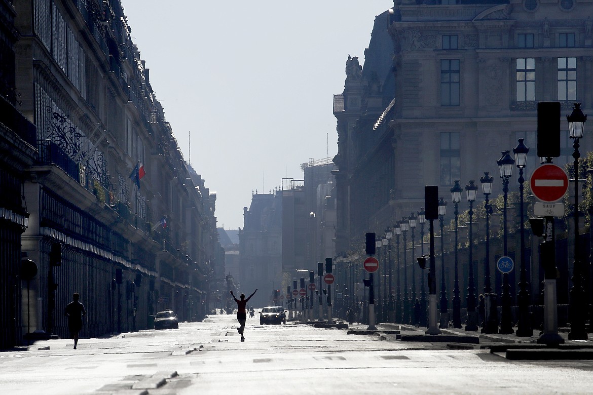 A woman stretches as she crosses the empty Rivoli street during a nationwide confinement to counter the Covid-19, in Paris, Sunday, April 5, 2020. The new coronavirus causes mild or moderate symptoms for most people, but for some, especially older adults and people with existing health problems, it can cause more severe illness or death. (AP Photo/Christophe Ena)