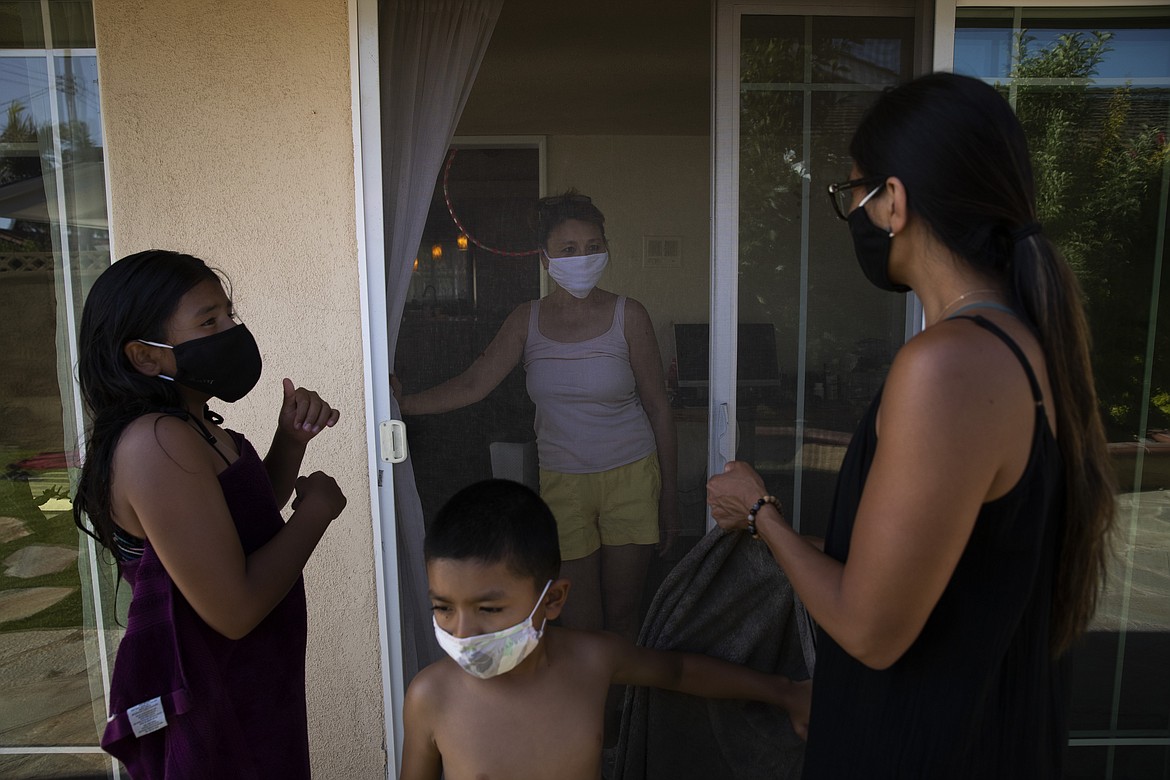 Nurse Jackie Vargas, right, stands with her children, Ava, left, and Kai, while chatting with her mother, Rose Matute, with a screen door between them at her mother's home in Lakewood, Calif., Saturday, July 11, 2020. The 39-year-old nurse, who works in St. Jude Medical Center's COVID-19 unit, doesn't hug her mother-in-law, who is taking care of her children. Through a glass door, she visits her own mom. (AP Photo/Jae C. Hong)