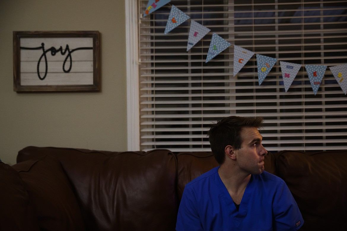 Spencer Cushing, a 29-year-old nurse who works in St. Jude Medical Center's COVID-19 unit, sits on a sofa in his home in Orange, Calif., Monday, July 13, 2020, after working a 12-hour shift. For the month of April, the Cushing family lived apart. Cushing spent his days and some of his nights at St. Jude's, as a nurse caring for "step-down" patients recovering from the most serious COVID-19 symptoms. (AP Photo/Jae C. Hong)