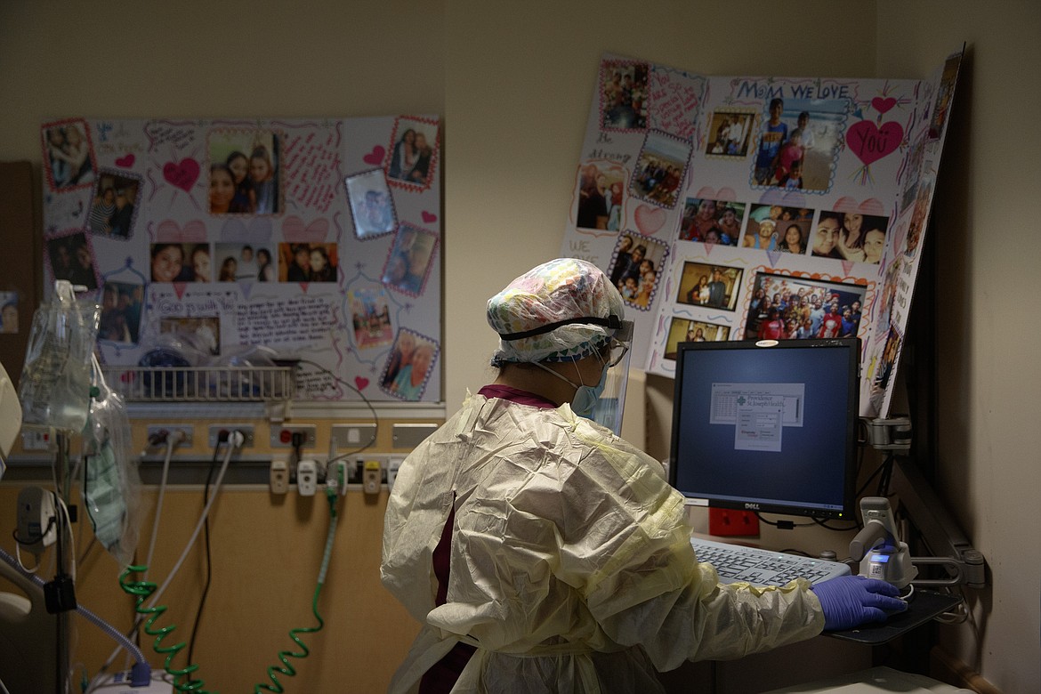 Nurse Sarvnaz Michel, 28, works on a computer while assisting a COVID-19 patient in a room with poster boards filled with family photos and get-well messages at St. Jude Medical Center in Fullerton, Calif., Friday, July 10, 2020. The 28-year-old's career has forced her to blur and blend her two lives. She agonizes over her every move in the hospital — "Did I put my gear on the right way, did I take it off the right way, did I touch something wrong accidentally?" — and locks her shoes in the car after her shifts. (AP Photo/Jae C. Hong)