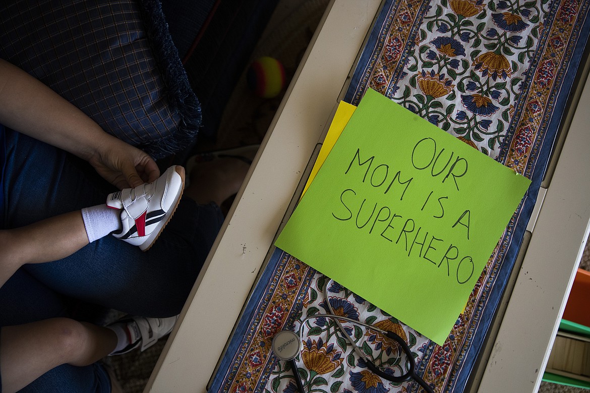Sarvnaz Michel, a nurse who works in St. Jude Medical Center's COVID-19 unit, puts shoes on her son, Arshan, next to a sign Michel's husband made to cheer her up Tuesday, July 14, 2020, in Garden Grove, Calif. Michel had just given birth to her youngest son, Arshan, prematurely and was supposed to return to work as a nurse on Valentine's Day. She took six weeks of unpaid maternity leave to buy time. She started a new job at St. Jude's in March, returning to a field very different from the one she had left before his birth. "I cry almost every night," she said. "If it was only about me, it would be a different story." (AP Photo/Jae C. Hong)