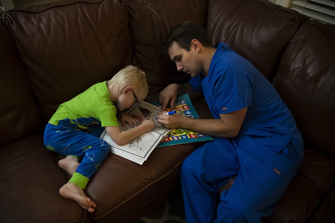 Spencer Cushing, a 29-year-old nurse who works in St. Jude Medical Center's COVID-19 unit, helps his 3-year-old son, James, color animation characters in Orange, Calif., Monday, July 13, 2020, after working a 12-hour shift at the hospital. For the month of April, the Cushing family lived apart. Cushing spent his days and some of his nights at St. Jude's, as a nurse caring for "step-down" patients recovering from the most serious COVID-19 symptoms. (AP Photo/Jae C. Hong)