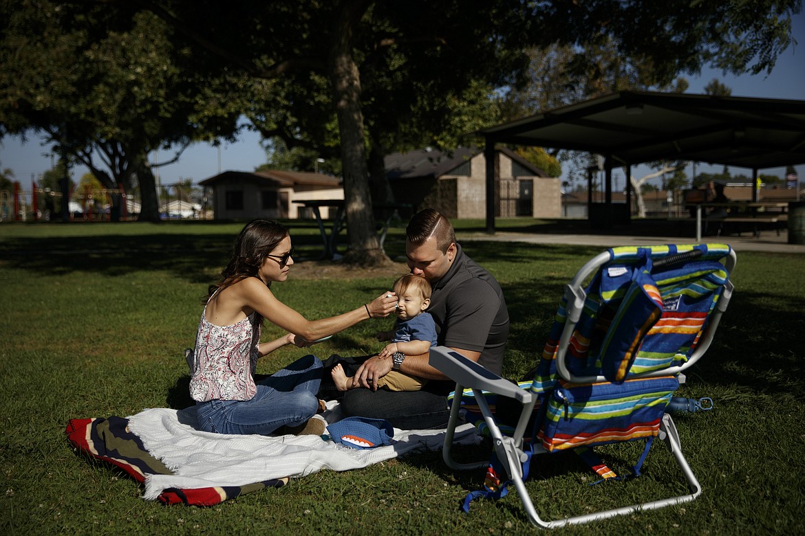 Nurse Michele Younkin, left, feeds her 7-month-old son, Jackson, as husband, Cody, gives him a kiss in a park on her day off in Garden Grove, Calif., Wednesday, Aug. 5, 2020. On the fifth day after her patient died of the coronavirus, Younkin's voice breaks as she sits cross-legged on a blanket during a sunny day in the park with her husband and giggling infant son. She had watched a man die — her first COVID-19 patient to pass on her watch. She had taken off her PPE, murmured to herself, "this never gets easier," and sobbed as she washed her hands. (AP Photo/Jae C. Hong)