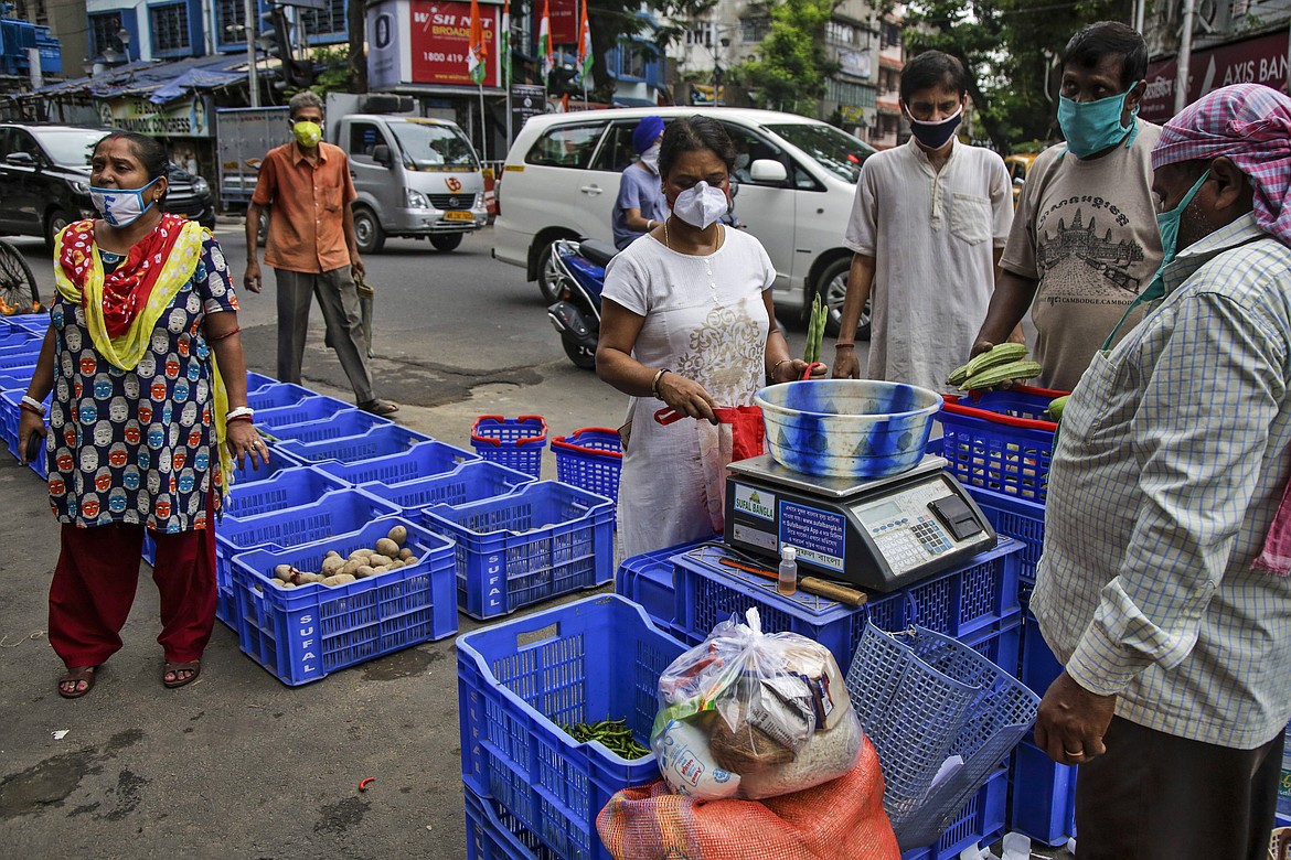 People wearing masks as a precaution against the coronavirus buy vegetables in Kolkata, India, Tuesday, July 21, 2020. With a surge in coronavirus cases in the past few weeks, state governments in India have been ordering focused lockdowns in high-risk areas to slow down the spread of infections. (AP Photo/Bikas Das)