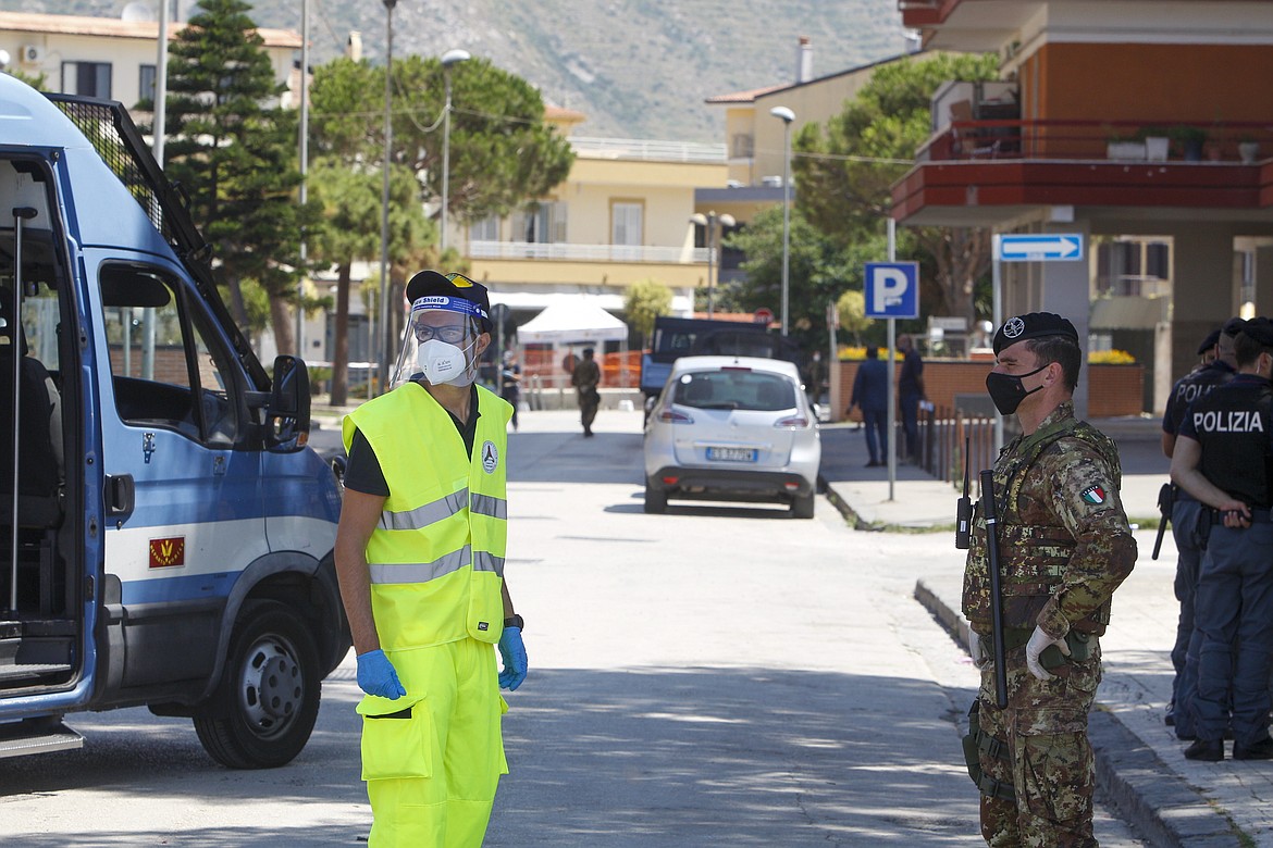 Civil protection and army officers stand at a road block in front of an apartment complex where dozens of COVID-19 cases have been registered among a community of Bulgarian farm workers, in Mondragone, in the southern Italian region of Campania, Friday, June 26, 2020. The governor of the region is insisting that the farm workers should stay inside for 15 days, not even emerging for food, and that the national civil protection agency should deliver them groceries. (AP Photo/Riccardo De Luca)