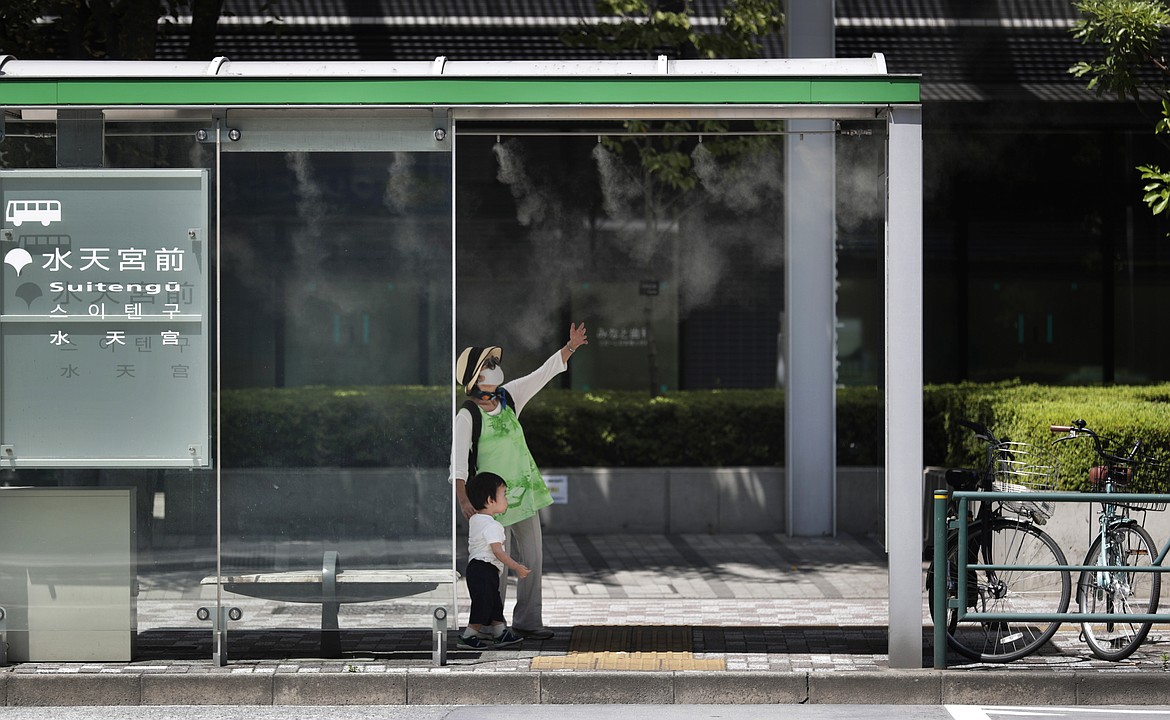 A woman wearing a face mask to protect against the coronavirus feels misting provided at a bus stop while talking with her grandson in Tokyo Thursday, Aug. 20, 2020. (AP Photo/Hiro Komae)