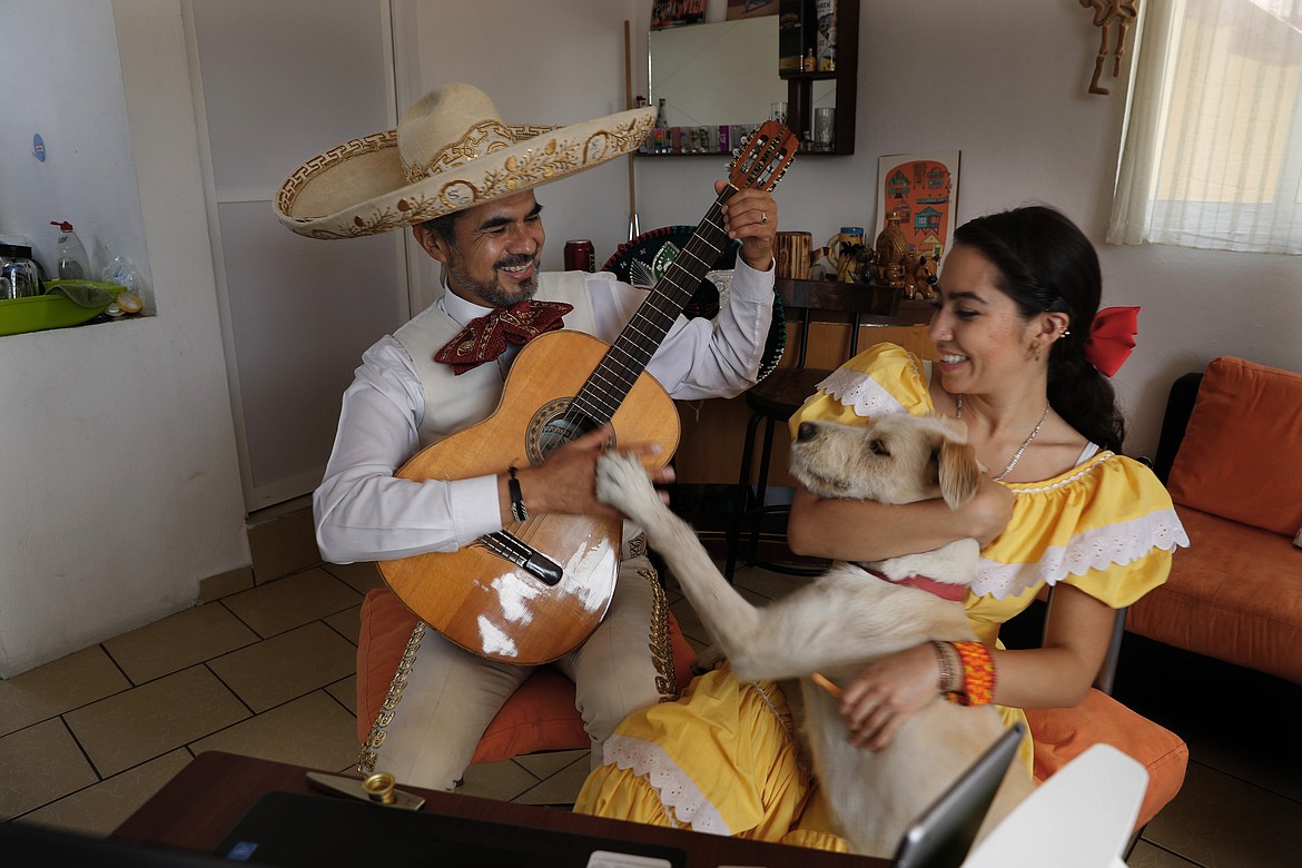 The Mariachi Duo Villa Maria, Sergio Carpio, left, and Melissa Villar, accompanied by their dog Güiro, perform via the internet for a client during mothers’ day, from their apartment in Mexico City, Sunday, May 10, 2020. The duo is performing Mariachi serenades remotely as a way to circumvent the collapse of their livelihood caused by the new coronavirus pandemic lockdown. The duo charges the equivlant of $30 per serenade that can be payed to their bank account via direct deposit. (AP Photo/Marco Ugarte)