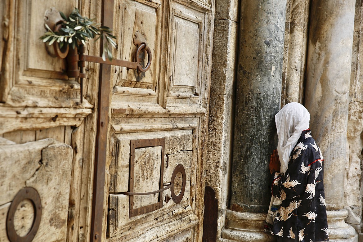 A woman prays in front of the closed Church of the Holy Sepulchre, a place where Christians believe Jesus Christ was buried, as a palm hangs on the door, in Jerusalem's Old City, Sunday, April 5, 2020. The traditional Palm Sunday procession was cancelled due to restrictions imposed to contain the spread of the coronavirus. (AP Photo/Ariel Schalit)