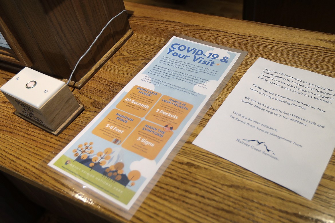 Signs at the reception desk at the National Park Inn at Longmire offer tips to prevent the spread of the COVID-19 virus and ask that guests limit use of a sitting area to 10 people or fewer, at Mount Rainier National Park, Wednesday, March 18, 2020, in Washington state. Most national parks are remaining open during the outbreak of the new coronavirus, but many are closing visitor centers, shuttles, lodges and restaurants in hopes of containing its spread. (AP Photo/Ted S. Warren)