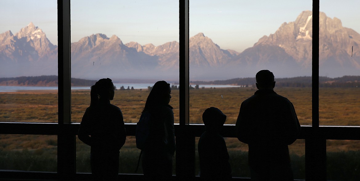 FILE - In this Aug. 28, 2016 file photo visitors watch the morning sun illuminate the Grand Tetons from within the Great Room at the Jackson Lake Lodge in Grand Teton National Park north of Jackson, Wyo. On Tuesday, March 24, 2020, the National Park Service announced that Yellowstone and Grand Teton National Parks would be closed until further notice, and no visitor access will be permitted to either park. (AP Photo/Brennan Linsley,File)