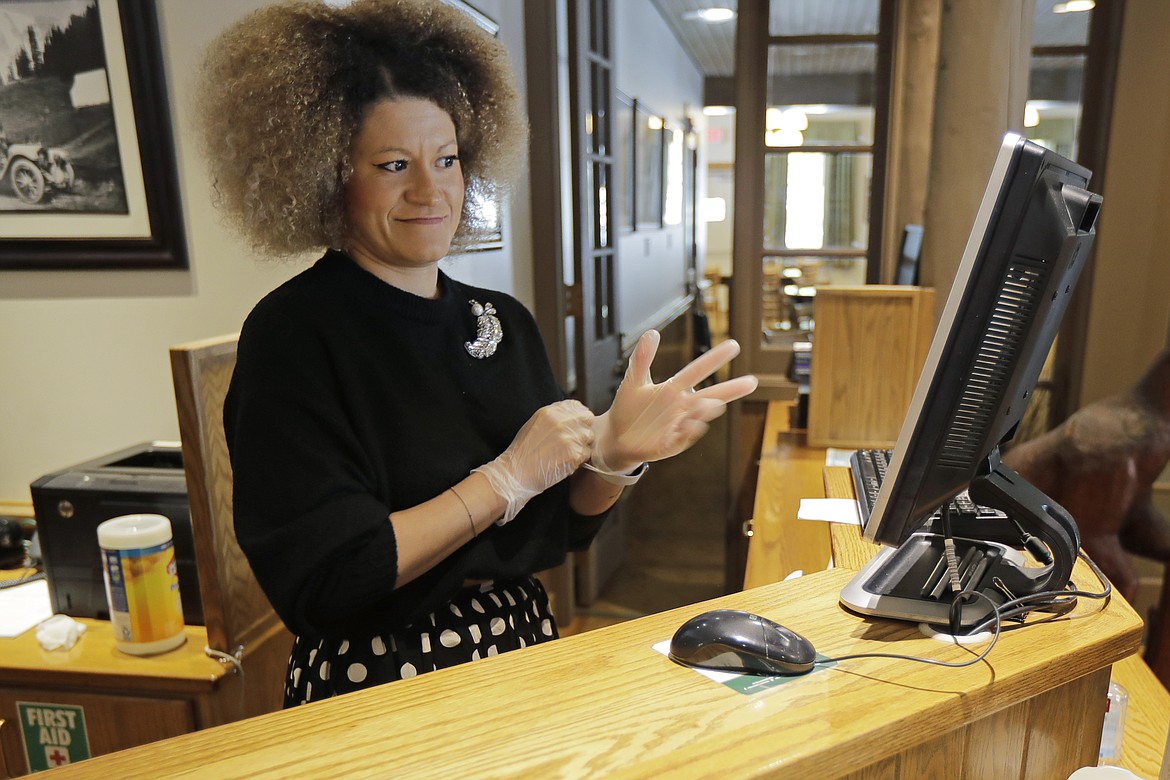Evelyn Waruszewski puts on gloves as she works at a reception desk at the National Park Inn at Longmire at Mount Rainier National Park, Wednesday, March 18, 2020, in Washington state. Most national parks are remaining open during the outbreak of the new coronavirus, but many are closing visitor centers, shuttles, lodges and restaurants in hopes of containing its spread. The restaurant at the inn is only offering food orders to-go. (AP Photo/Ted S. Warren)