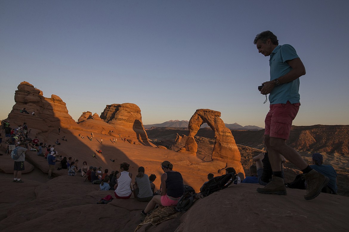 FILE - In this Sept. 8, 2016, file photo, people gather to watch the sunset at Delicate Arch in Arches National Park near Moab, Utah. Most of America's national parks remain open as some of the last refuges for weary Americans sick of being stuck at home, but many are closing visitor centers, shuttles, lodges and restaurants in hopes of containing the spread of the coronavirus. (Spenser Heaps/The Deseret News via AP, File)