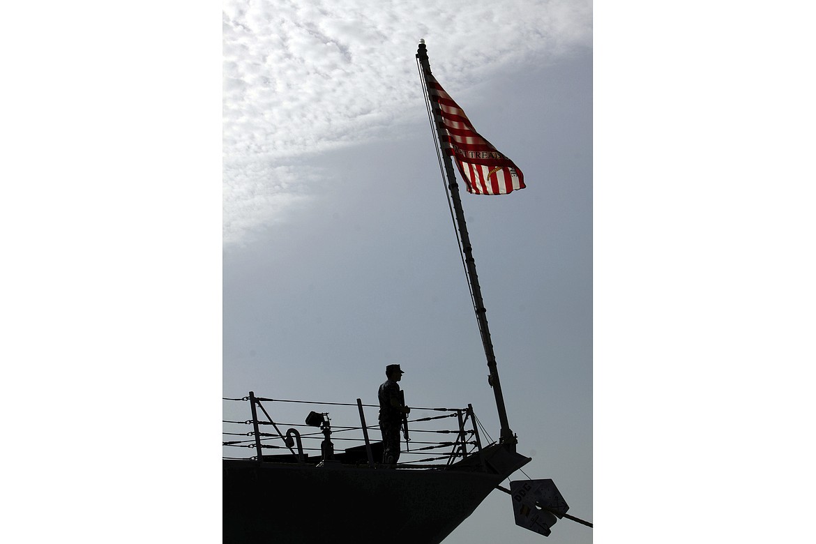 FILE- In this Jan. 12, 2012 file photo, a U.S. Navy sailor is seen by the American flag during a change-of-command ceremony Taboard the destroyer USS Kidd docked in Muharraq, Bahrain. The Navy says another warship at sea has reported a coronavirus outbreak and is returning to port. In a written statement, the Navy said Friday at least 17 members of the crew of the USS Kidd have tested positive for the virus. The destroyer was operating in the Caribbean Sea.  (AP Photo/Hasan Jamali)