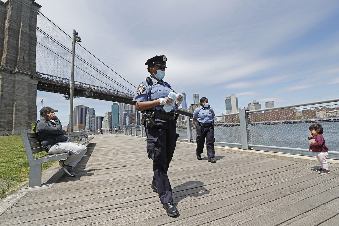 A youngster approaches a team of New York City police officers as they walk with face masks to hand out to anyone who needs or asks for one during the current coronavirus outbreak, Sunday, May 17, 2020, in Brooklyn Bridge Park in New York. (AP Photo/Kathy Willens)