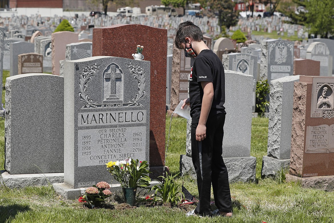 Joseph Scaduto, 12, pours water onto flowers he and family members planted at the grave of relatives at Calvary Cemetery on Mother's Day, Sunday, May 10, 2020, in New York. The cemetery had been closed due to concerns over the spread of the new coronavirus, but opened its gates for several hours Sunday to allow families to visit the graves of loved ones. (AP Photo/Kathy Willens)