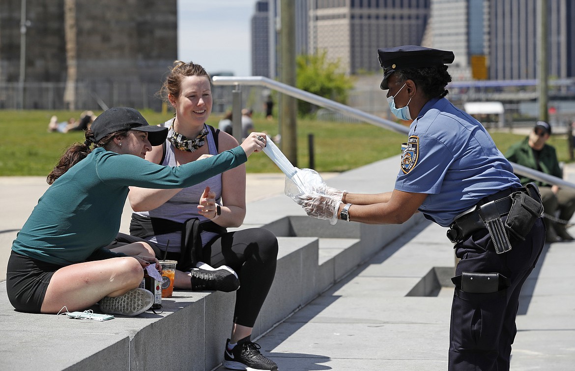 New York Police Department School Safety officer Bynoe, right, hands out face masks to women at Brooklyn Bridge Park during the coronavirus pandemic, Sunday, May 17, 2020, in New York. (AP Photo/Kathy Willens)