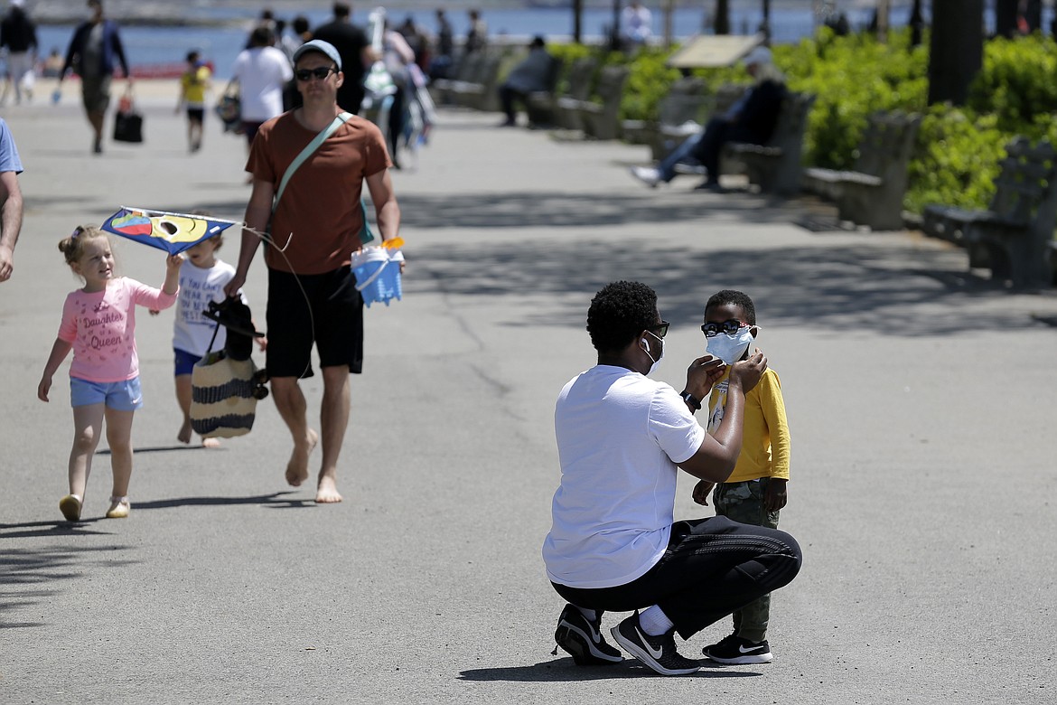 A man adjusts a child's mask before heading out to the sand at Orchard Beach in the Bronx borough of New York, Sunday, May 17, 2020. Parks, boardwalks and beaches attracted some crowds this weekend, though city beaches aren't officially open and won't be for the upcoming Memorial Day weekend.  (AP Photo/Seth Wenig)