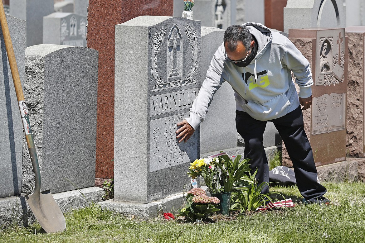 Anthony Garrita touches his great-aunt Concietta Sireci's gravestone at Calvary Cemetery on Mother's Day after planting flowers, Sunday, May 10, 2020, in New York. Garrita's grandparents and other relatives are also buried there. The cemetery had been closed due to concerns over the spread of coronavirus, but opened its gates for several hours Sunday to allow families to visit the gravesites of loved ones. (AP Photo/Kathy Willens)
